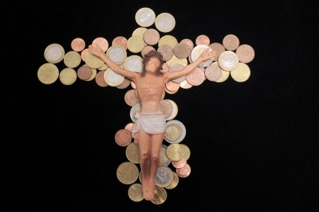 coins formed in the shape of a cross and a Jesus figure with outstretched arms sits on top of them